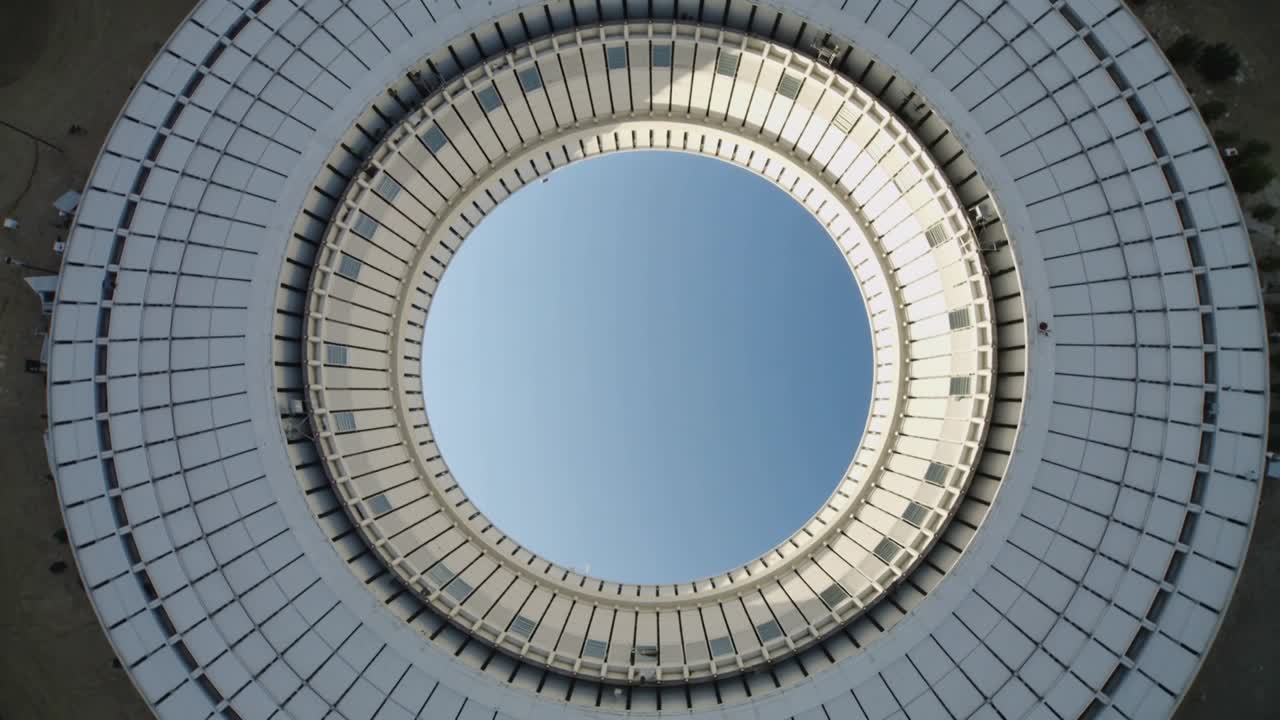 Drone rotante che svela un oculo e un anello interno su un edificio in piazza, enfatizzando una fascia illuminata dal sole.