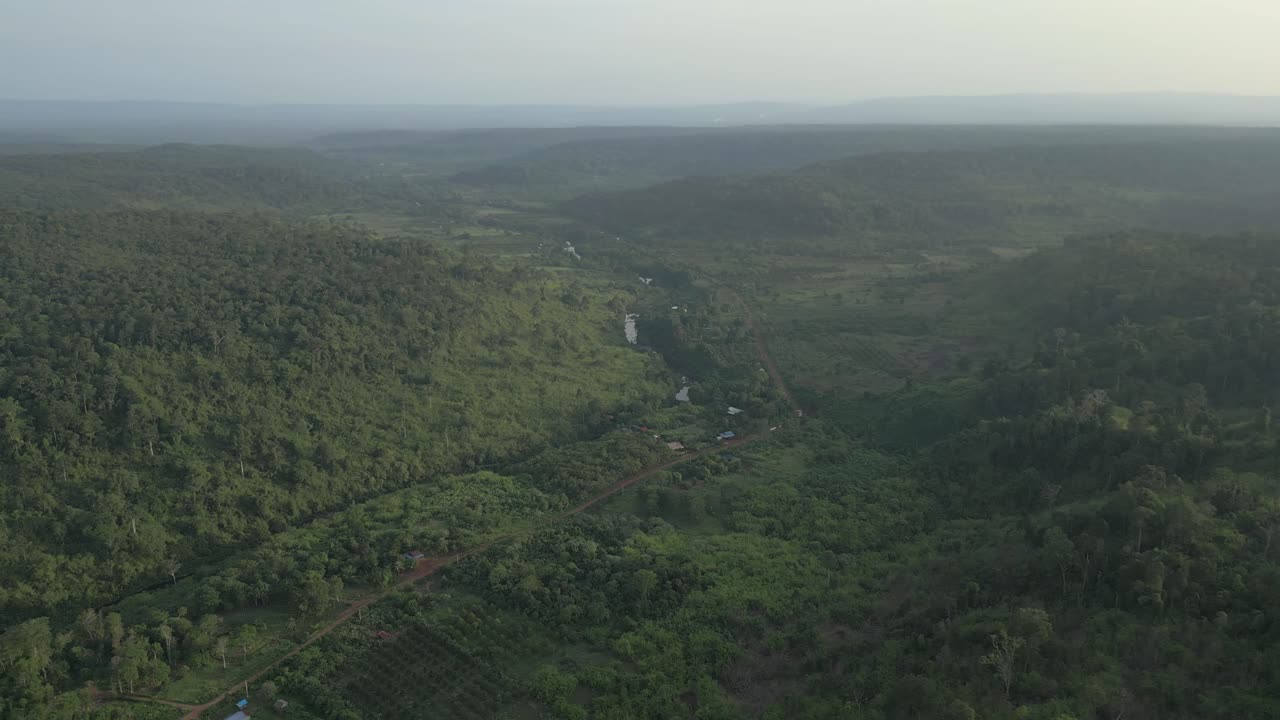 Drone orbiting above a lush valley, circling farmland and forest in soft sunset light.
