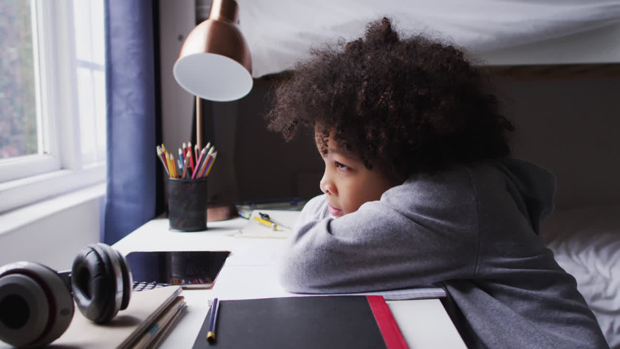 Ragazza multietnica seduta alla scrivania che guarda fuori dalla finestra