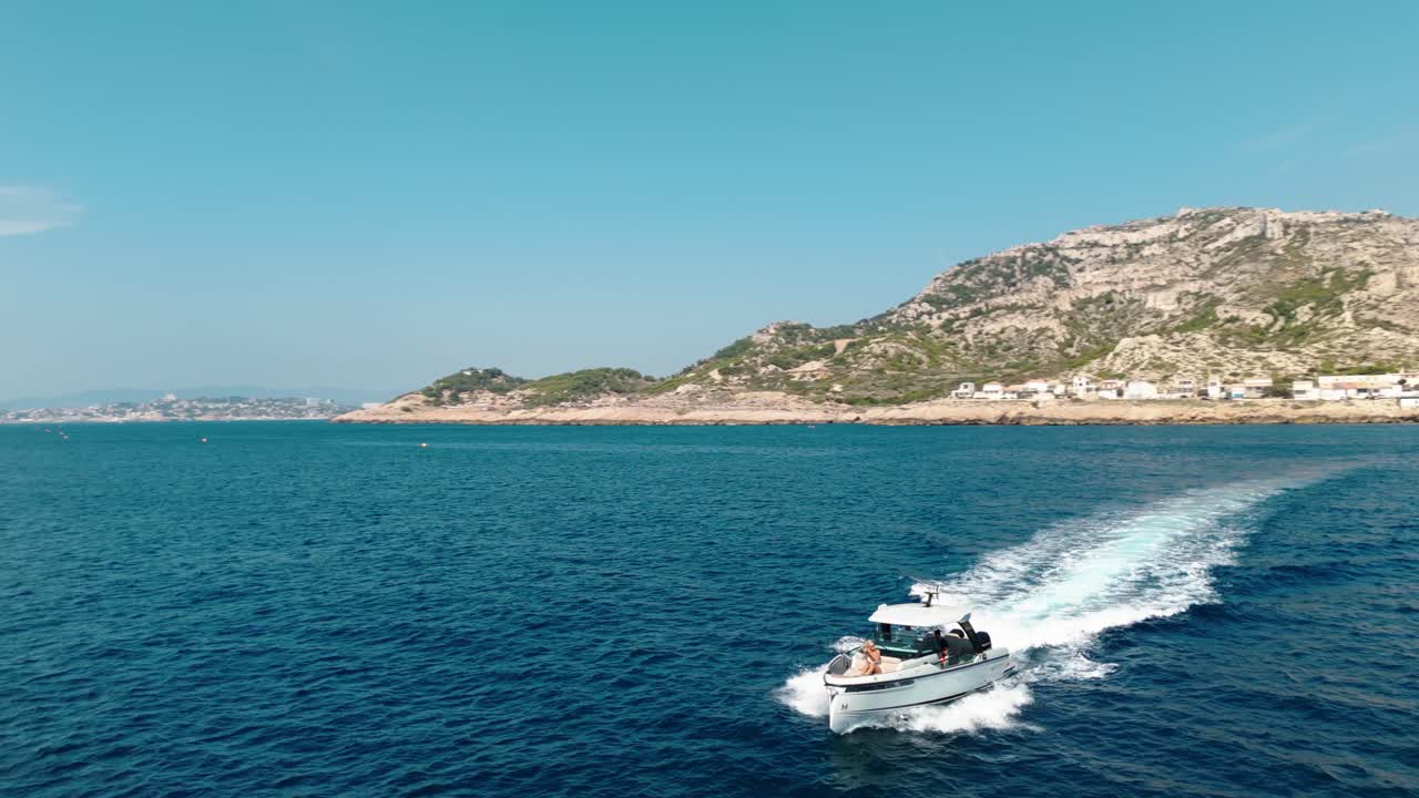 A sleek boat glides through crystal-clear Mediterranean waters, with the picturesque French coastline as a stunning backdrop of natural beauty and elegance.