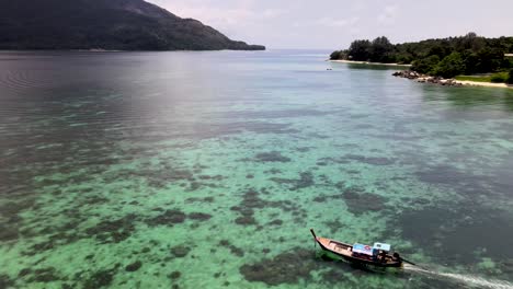 Flying-over-moving-longtail-asian-local-boat-in-turquoise-sea-of-tropical-island