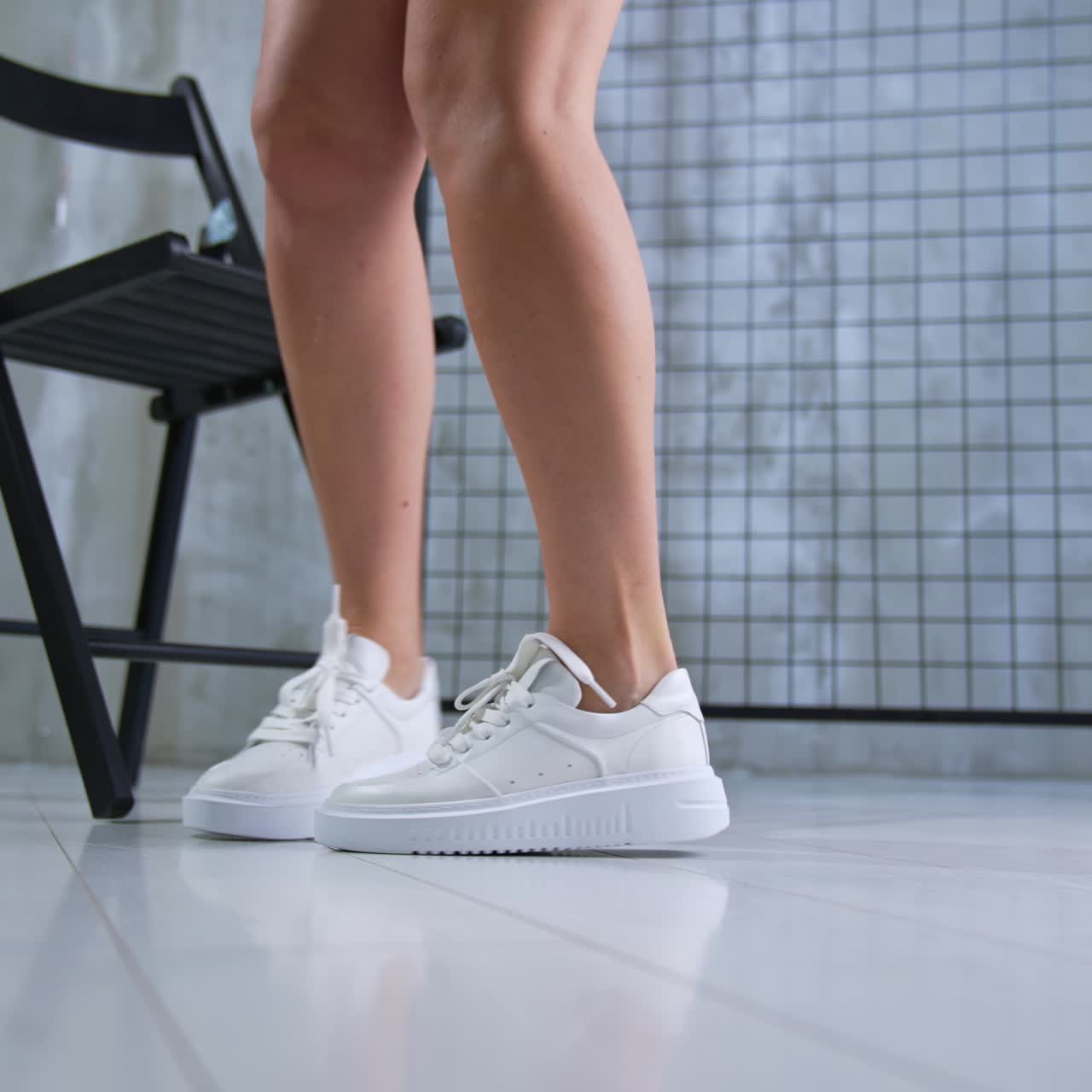 Female wears white stylish sneakers with laces. Model in bicycle shorts and white shirt demonstrates nice stylish shoes in studio