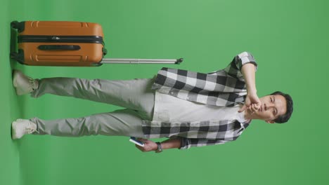 full body of asian male traveler with luggage and passport looking at camera and showing thumbs down gesture in the green screen background studio