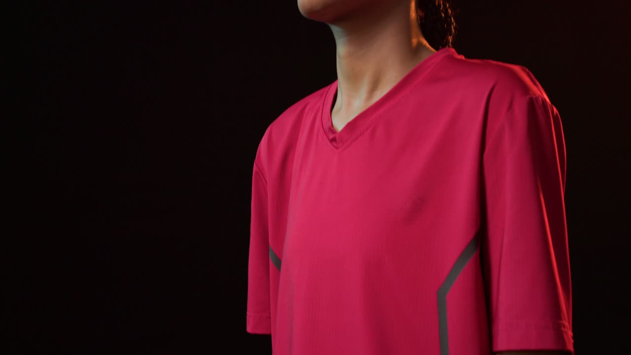 Portiere donna afroamericana che alza le braccia, con la telecamera che si muove verso l'alto in studio mostrando la maglia rossa e i guanti.