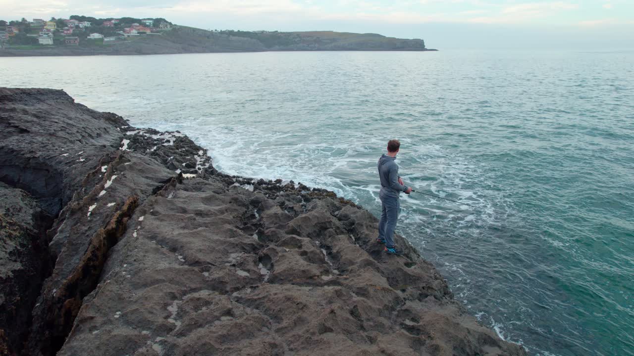 pescador masculino en órbita en la costa cantábrica con olas rompientes en isla, un pueblo de cantabria, españa