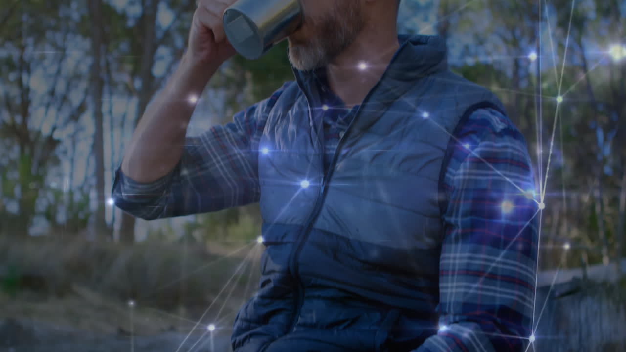 adult man sipping from steel mug at forest clearing, glowing tech network nodes floating around him