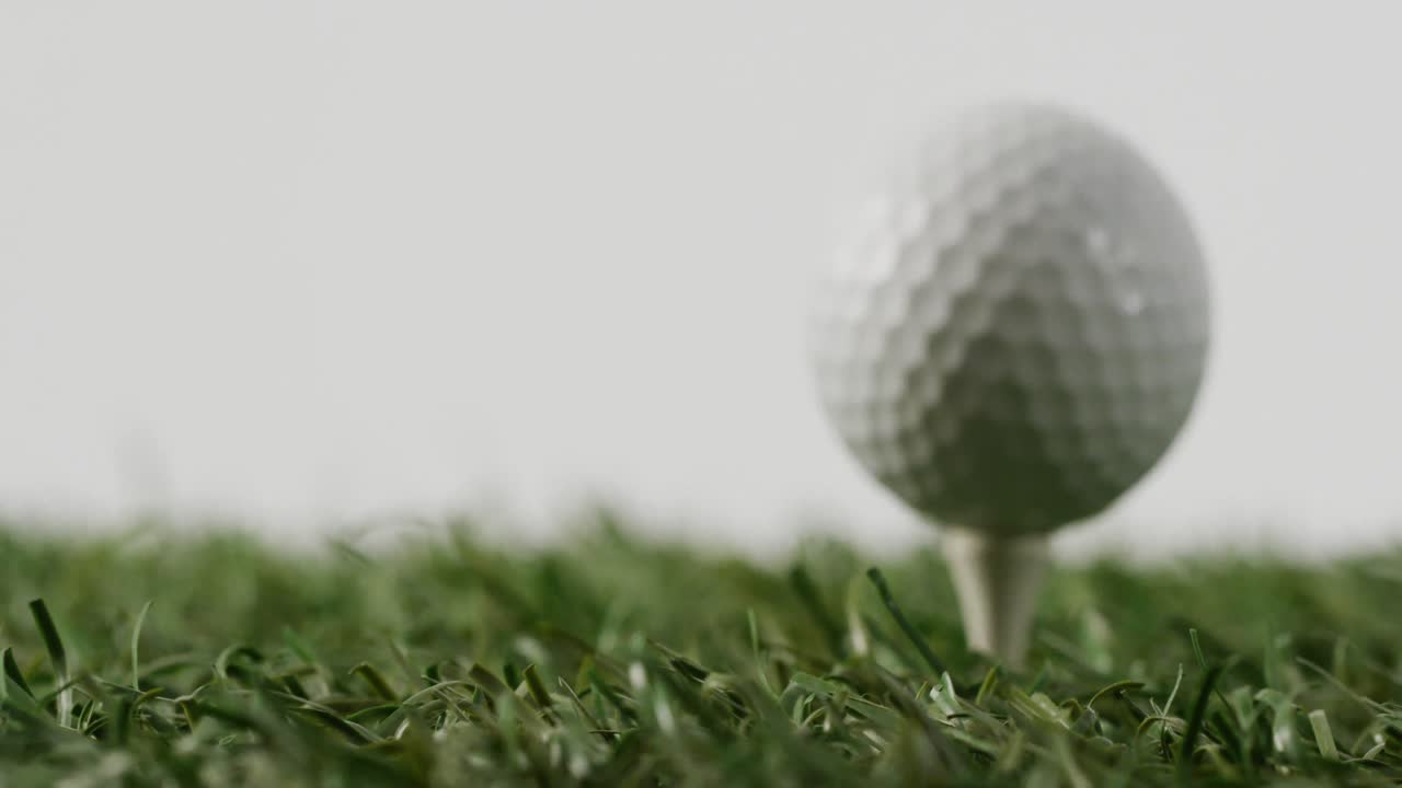 Close-up van golftee en bal op gras en witte achtergrond, met ruimte voor tekst, in slow motion.