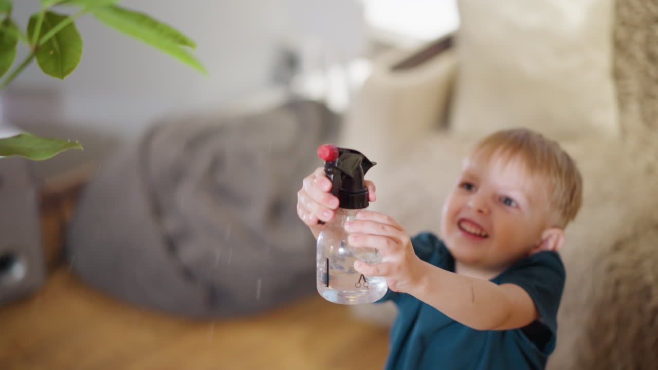 Happy boy watering indoor plant using spray bottle, smiling and enjoying playful learning activity, showing excitement, joy, and care for greenery inside cozy home environment with comfort