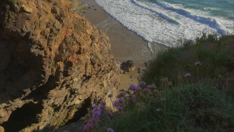 Staring-down-from-high-cliffs-as-waves-roll-onto-beach,-high-angle