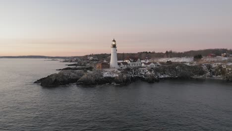 lighthouse flashing above rocky coastal outcrop, winter sunrise, stationary aerial