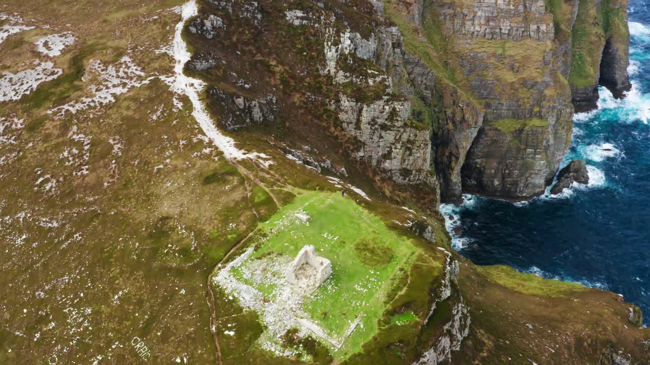 Top-down orbit of Ireland’s Horn Head with adventurers exploring the grassy summit beside The Napoleonic Tower and sea behind