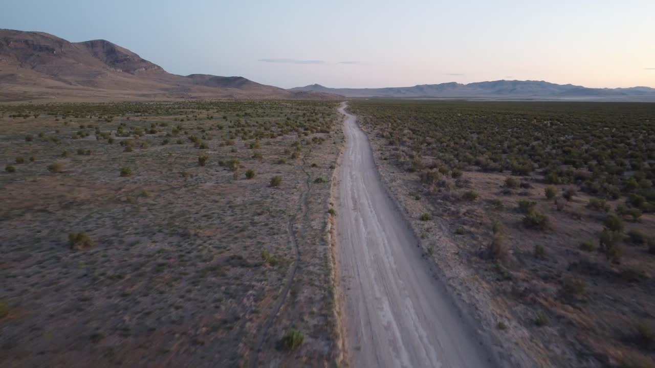 Aerial pass over a dusty desert track toward canyon ridges during sunset, highlighting Utah’s rugged landscape and offering strong cinematic visuals