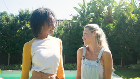 two female friends smiling and chatting by poolside on sunny day
