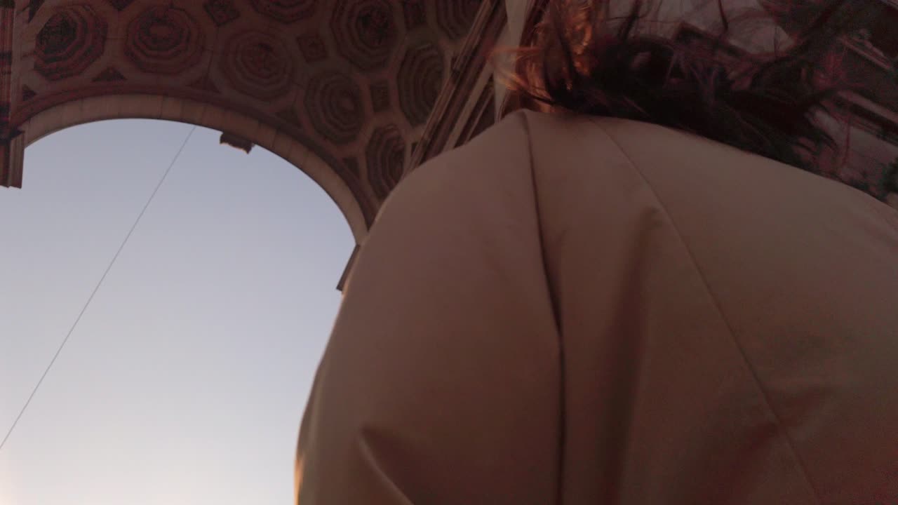 Woman walks under Cinquantenaire Arch in warm sunlight