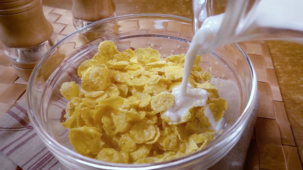 Knusprige gelbe Cornflakes in die Schale für ein köstliches Frühstück mit Milch am Morgen. Zeitlupe mit rotierender Kamerafahrt