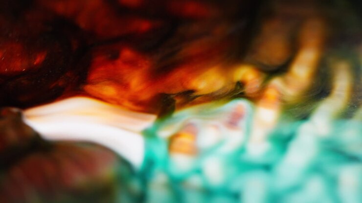 Macro shot of cyan, orange, black, and red ink flowing and mixing together, forming bubble-like shapes on the surface