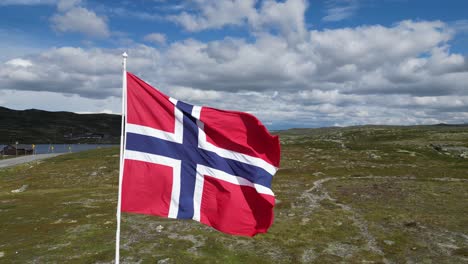 norwegian flag waving in the wind in hardangervidda national park, norway