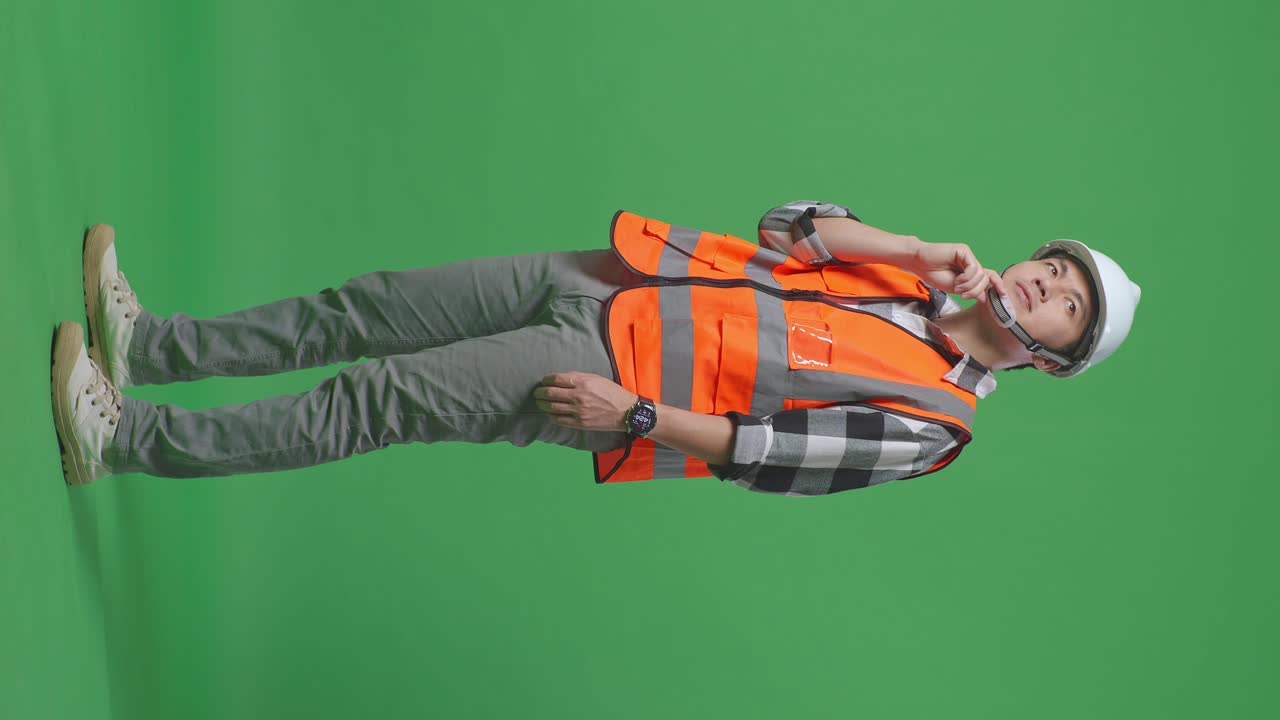 Full Body Side View Of Asian Male Engineer With Safety Helmet Thinking And Looking Around Then Raising His Index Finger While Standing In The Green Screen Background Studio
