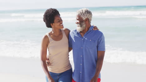 Happy-african-american-couple-walking-and-embracing-on-sunny-beach