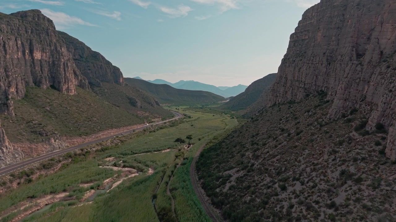 Aerial drone view of river valley between rocky mountains. Green vegetation winding river cliffs and distant hills create a dramatic natural landscape captured from above