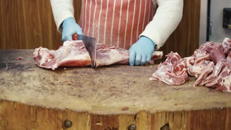 medium shot of a butcher hacking away at a large chunk of raw meat