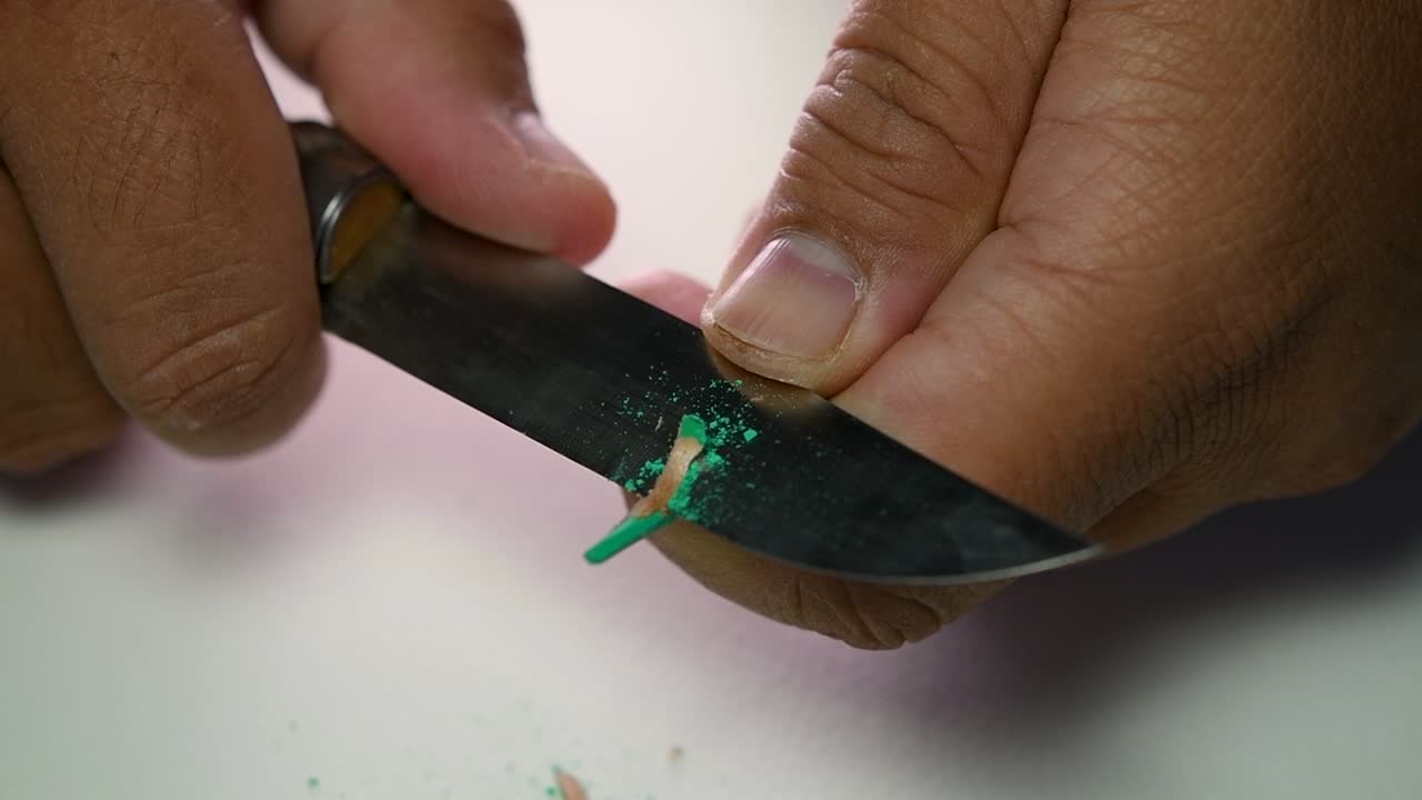Footage of hands slowly sharpening a pencil and some coloured pencils with a sharp knife
