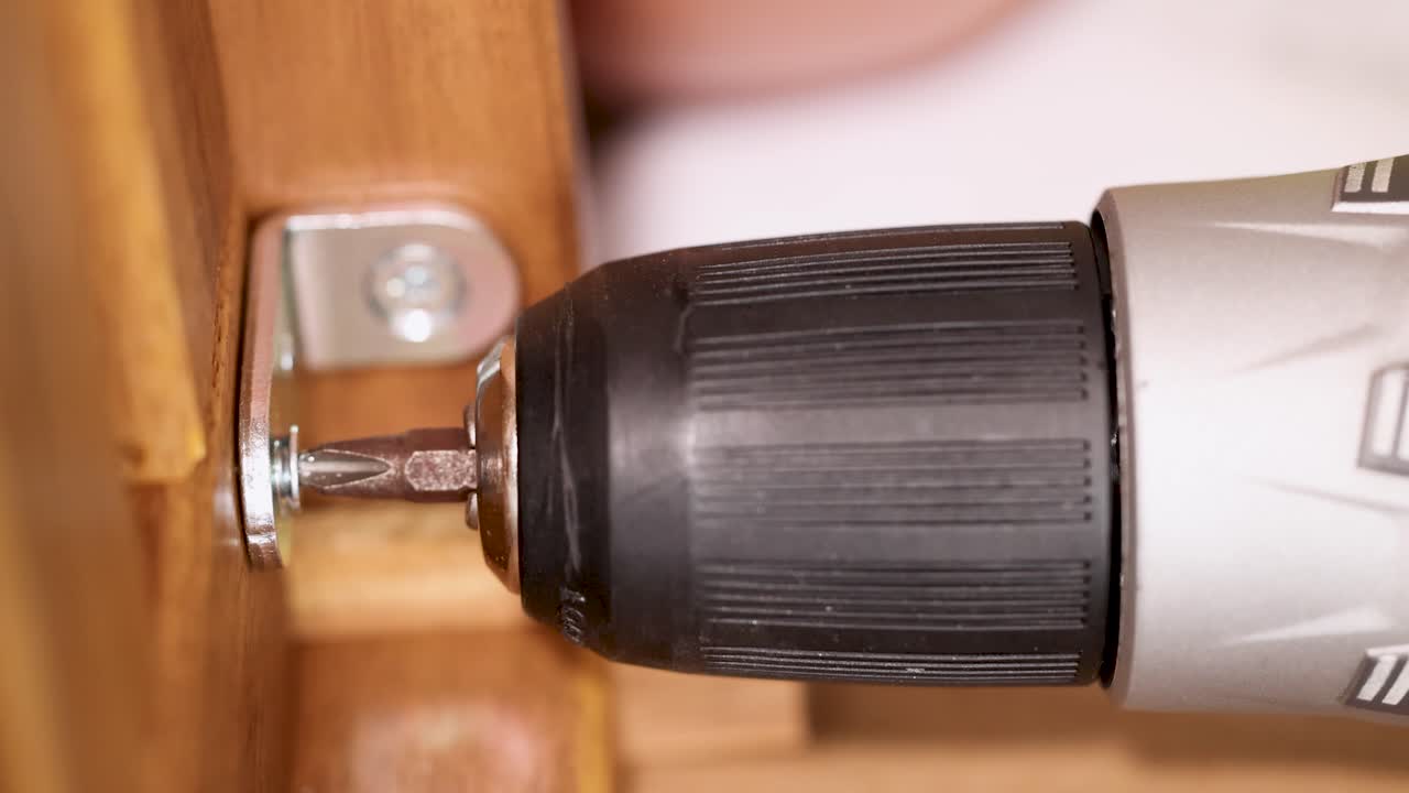 A power drill secures screws into wooden furniture, showcasing efficient assembly in a well-lit environment