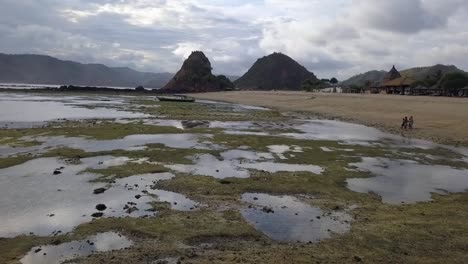 Boot-Bei-Ebbe-Am-Riff,-Einheimische-Kinder-Am-Strand,-Geheimnisvoller-Himmel,-Wolken,-Wunderbare-Luftaufnahme,-Flug-Rückwärts-Fliegen,-Drohnenaufnahmen,-Pantai-Kuta-Lombok,-Indonesien,-Filmisch-Von-Oben-Von-Philipp-Marnitz