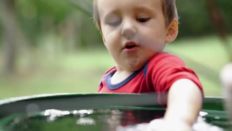 Niño-Pequeño-Caucásico-Jugando-Con-Juguete-De-Avión-De-Plástico-En-Un-Barril-Lleno-De-Agua,-Cámara-Lenta