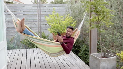 relaxing in hammock, man using smartphone and smiling on wooden deck