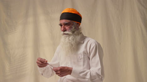 fotografía de estudio de un anciano sikh con barba atando tela para el turbante contra un fondo plano como secuencia parte 2 de 3