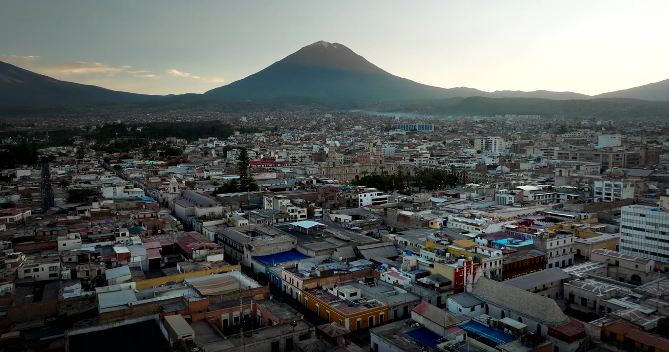 Arequipan valkoisen kaupungin siluetti Misti-tulivuoren kanssa auringonnousun aikaan kirkkaan taivaan alla, dronella kuvattu panoraama, joka esittelee tulivuoren kohoavan etäällä