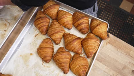 baker moves freshly baked croissants from one tray to another for cooling, slow motion top down 4k