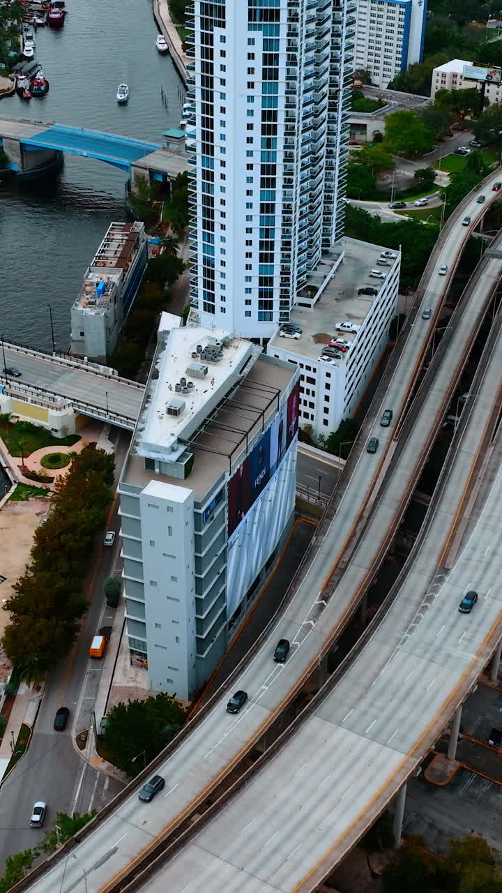 Rising above the ramified highway going along the narrow river in downtown. View of Miami, Florida, USA from top. Vertical video