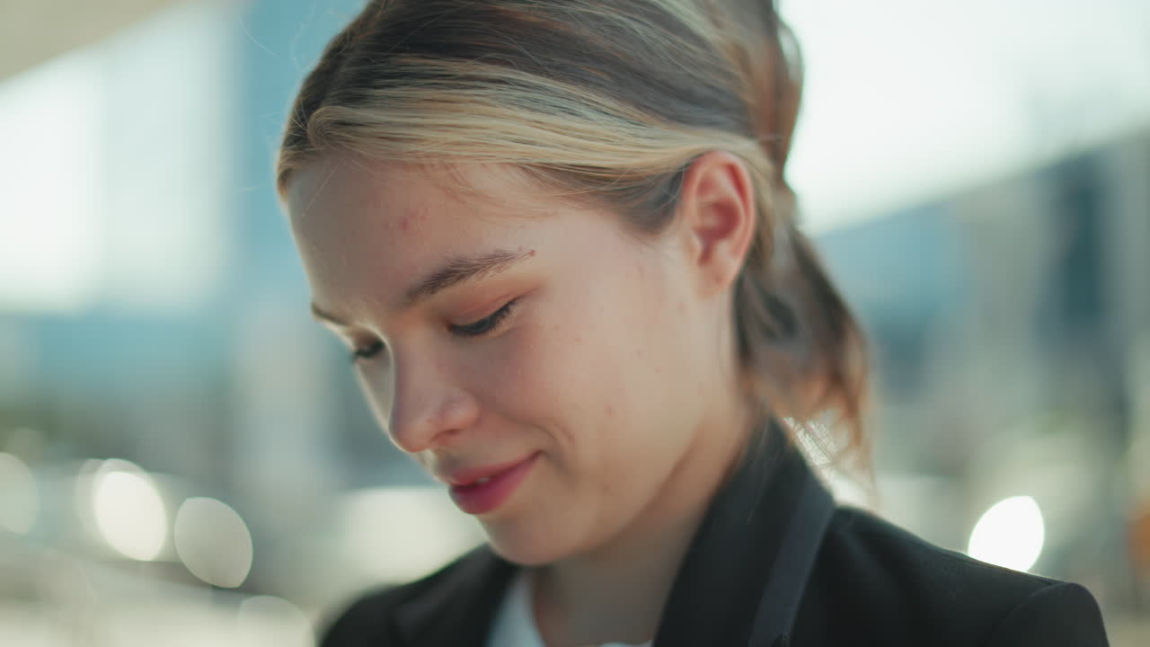 Close up of elegant lady with cat eyes wearing suit smiling warmly and staring at camera outdoors in professional setting with blurred urban background reflecting soft daylight