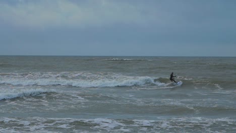 man engaged in kitesurfing, overcast winter day, high waves, baltic sea karosta beach , slow motion, distant wide shot