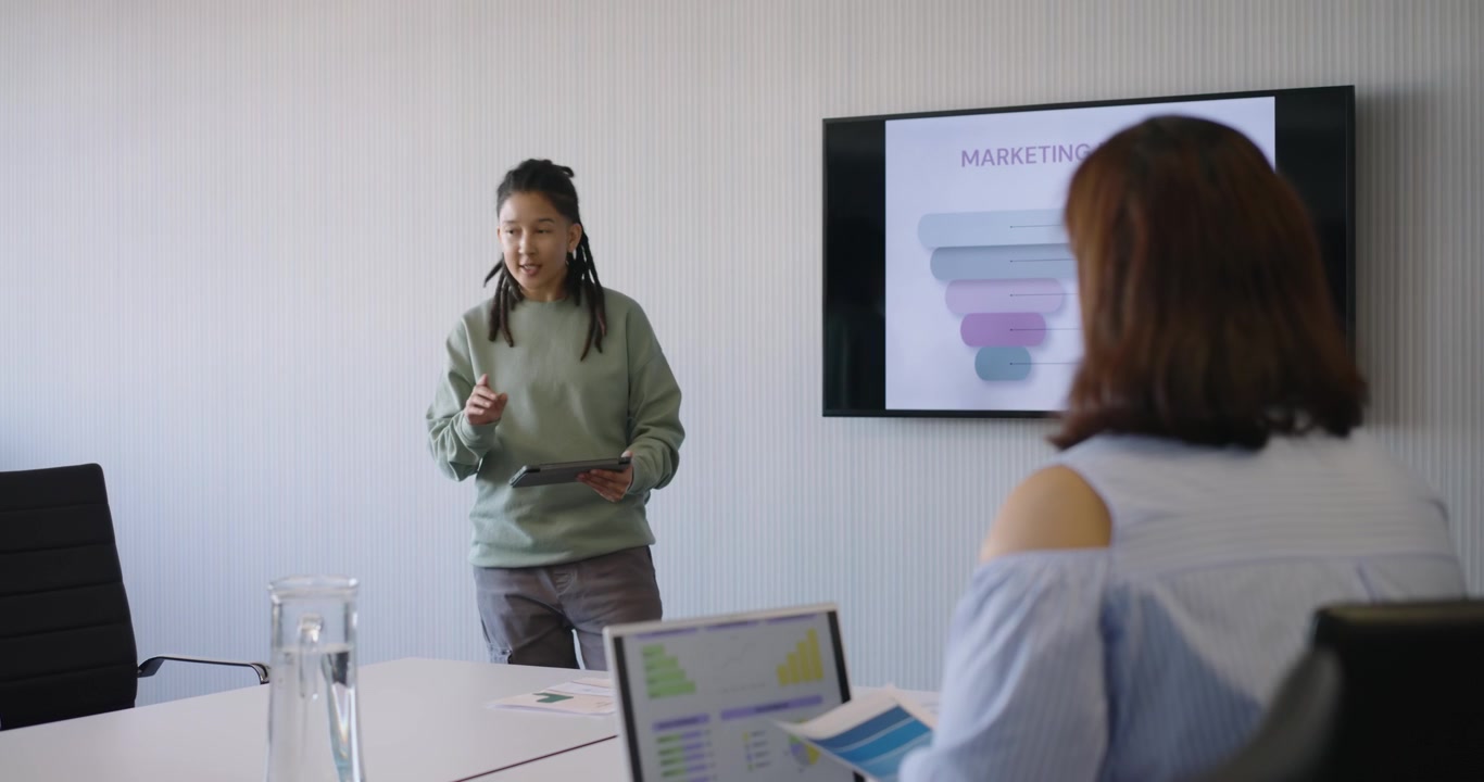 Donna che consulta un tablet, presenta un funnel di marketing mentre un collega non binario esamina i grafici al tavolo