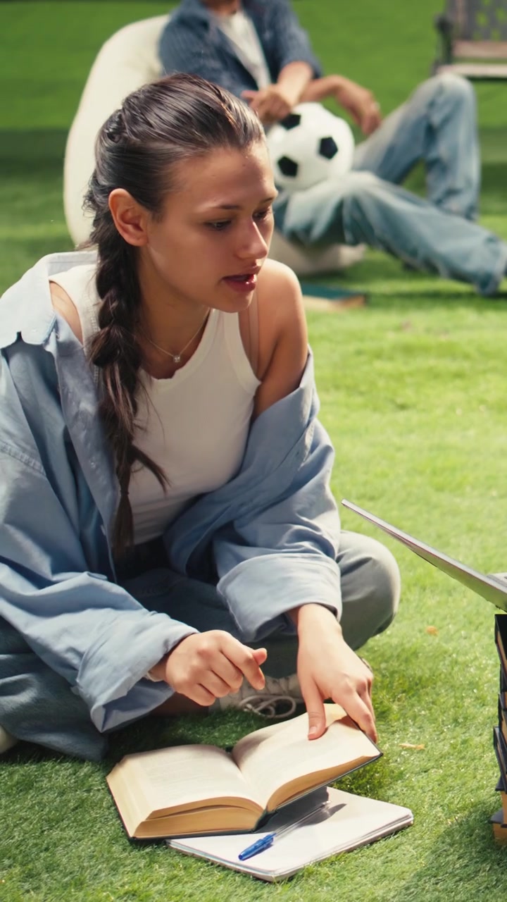 Vertical Video Classmates in study session sitting on grass with laptop placed on stacked books