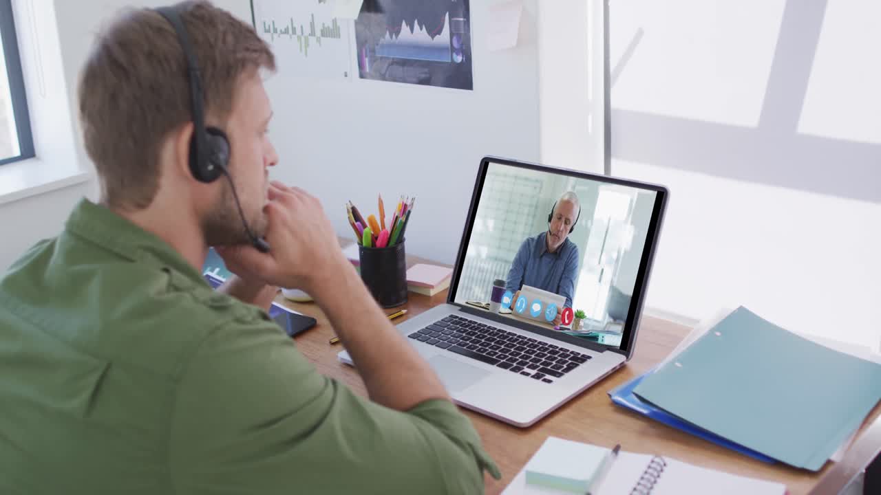 Kaukasisk mand bruger bærbar computer og telefonheadset på videoopkald med en mandlig kollega.