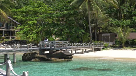 Model-in-a-white-dress-walking-over-a-wooden-bridge-on-a-tropical-island