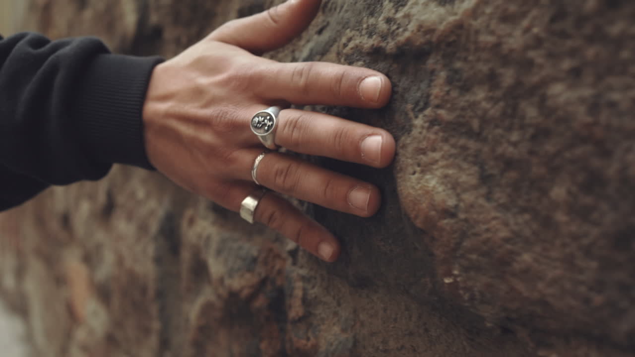 manos caucásicas con anillos de plata se arrastran, sintiendo la pared de piedra