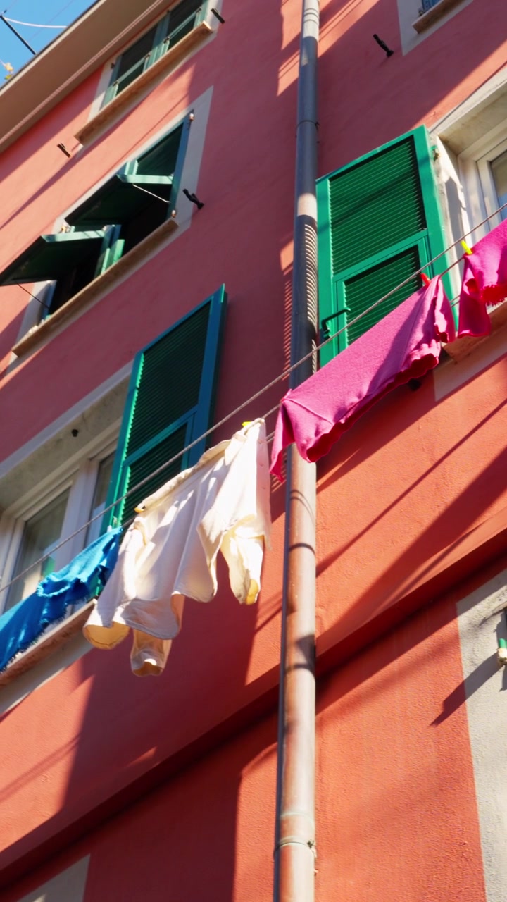 Bucato colorato ondeggia sui fili fuori da un edificio luminoso con persiane verdi alla luce del sole.