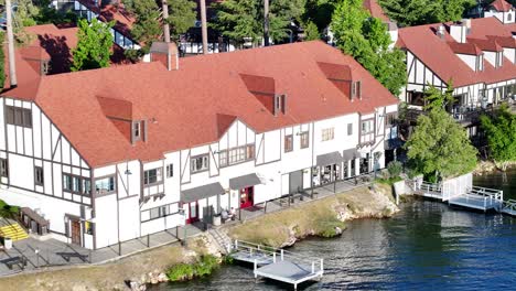 Edificios-De-Estilo-Alemán-En-El-Lago-Arrowhead-En-California-Durante-La-Puesta-De-Sol-Con-Barcos-Y-Muelles-Alrededor-De-La-Compresión-De-Teleobjetivo-De-Camiones-Aéreos