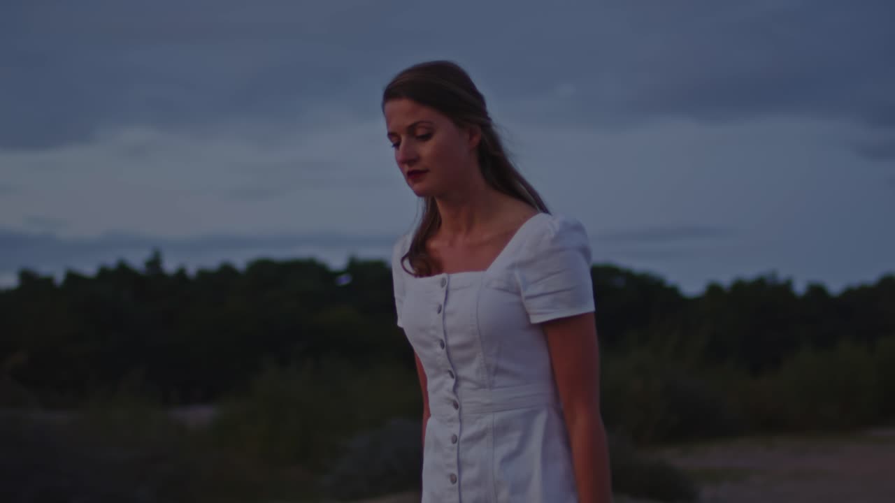 황혼에 모래 언덕을 걷는 매력적인 젊은 여자