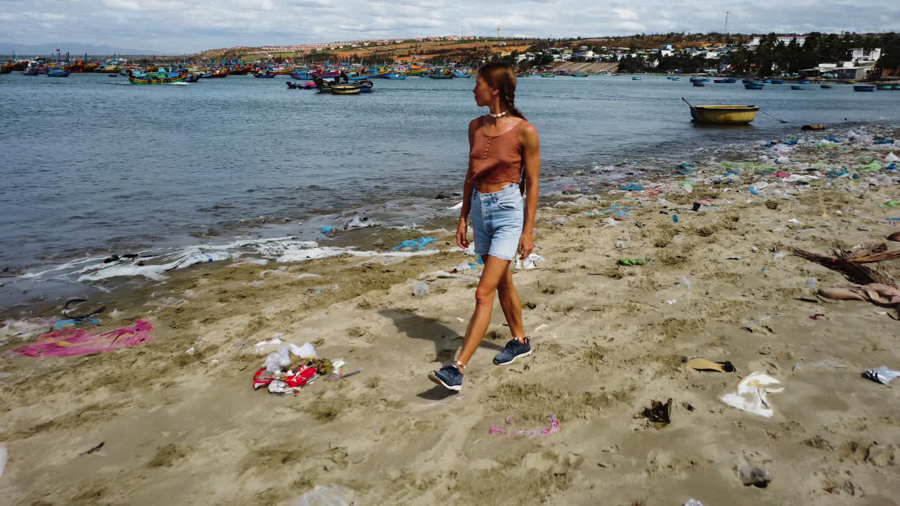 mujer delgada mirando en la costa de mui ne mientras camina en la playa con basura en vietnam