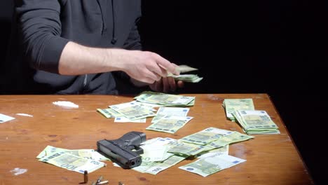 Traficante-De-Drogas-Contando-Dinero-En-La-Mesa-Con-Pistola,-Balas-Y-Cocaína