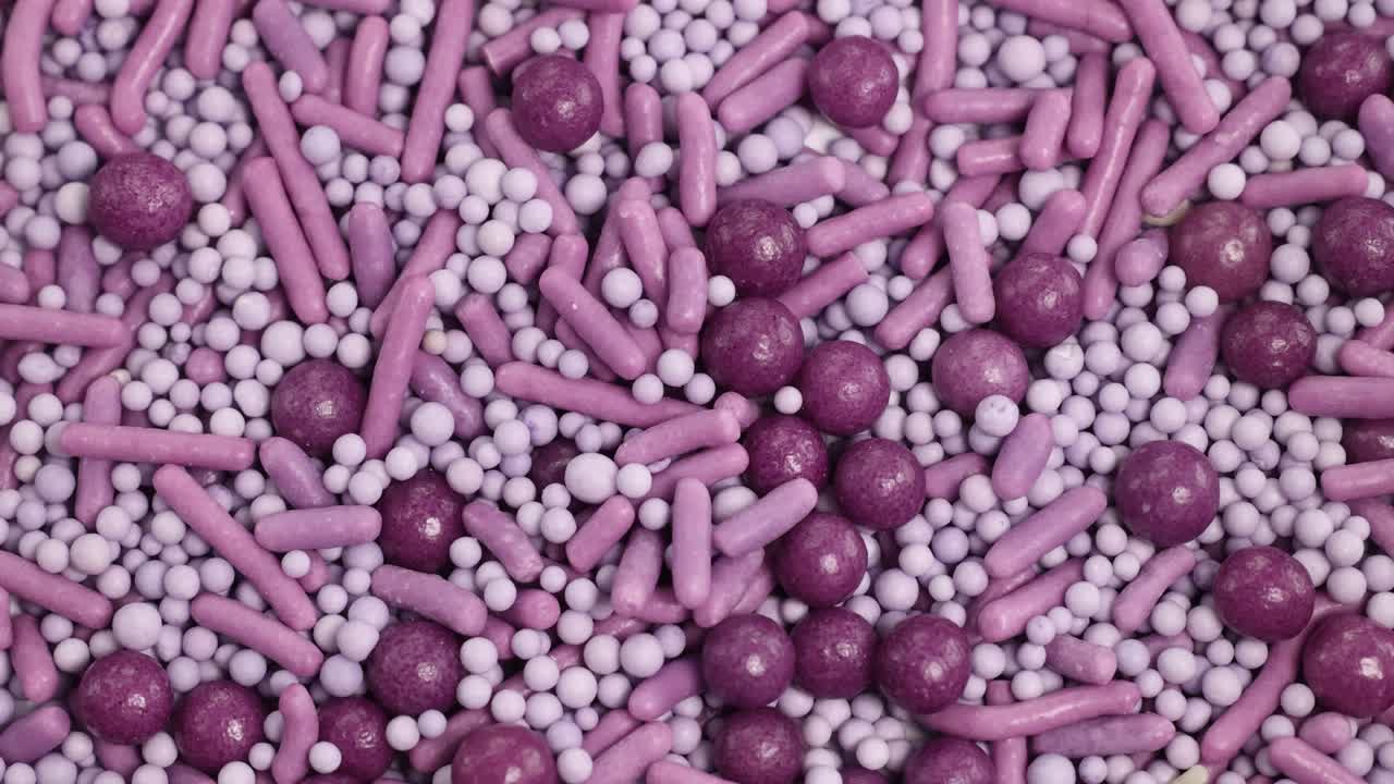 A spoon scoops vibrant purple candy sprinkles in a macro close-up, highlighting texture and color under bright lighting