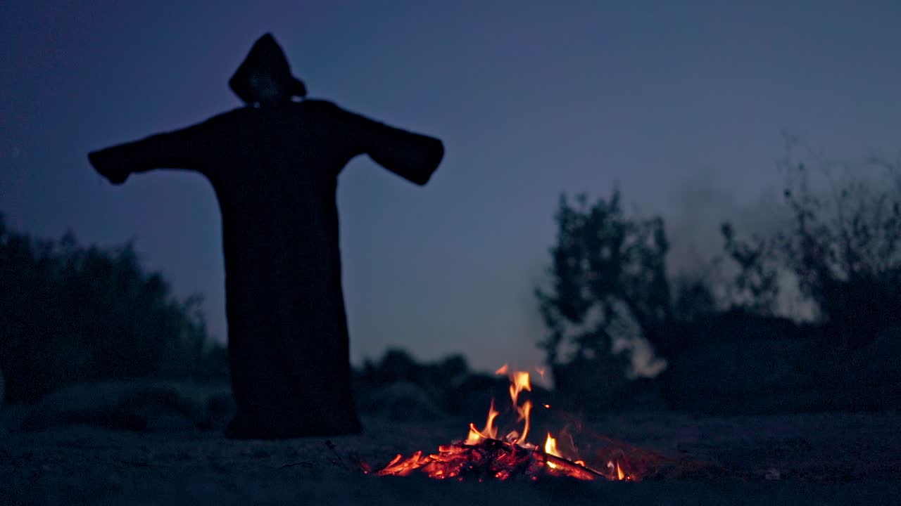 Scary figure in black mantle. Black witch in a mantle during ritual near fire