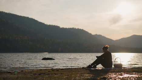 lady rests on picnic by lake at sunset. upset woman with food basket copes with negative emotions being alone on vacation. feeling of loneliness