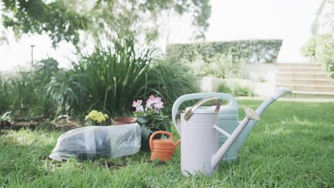 Close-up-of-watering-cans,-flowers-and-pots-in-sunny-garden,-slow-motion